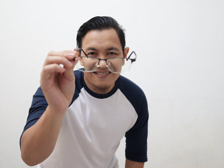 Portrait of Asian man smiling while adjusting his eyeglasses trying to see focus, eye sight trouble, blur vision, against white backgroundの写真素材