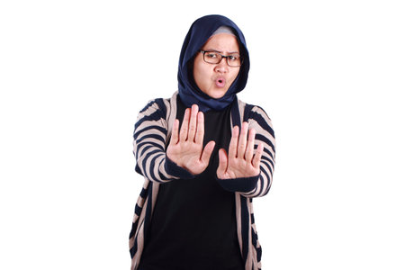 Asian muslim lady wearing hijab shows stop sign, prohibit forbid disallow something bad with palm hand gesture, isolated on whiteの写真素材