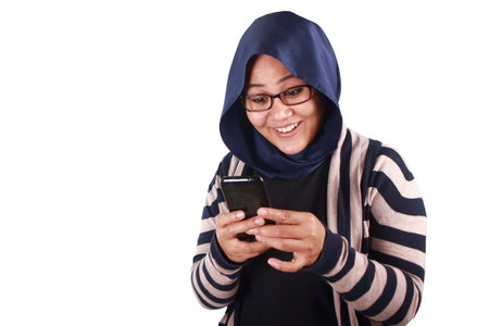 Portrait of young Asian muslim woman wearing hijab get good news on her phone, happy surprised expressionの写真素材