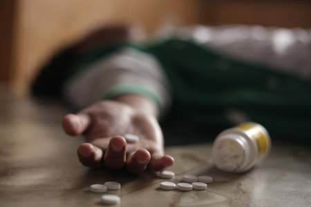 Anonymous man lying on the floor, unconscious or dead due to drugs abuse, focus on fingers with pillsの写真素材