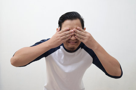 Portrait of funny young Asian man afraid worried expression with hands covering his eyes, against grey backgroundの写真素材
