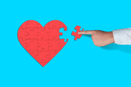 Persons hand put one piece of jigsaw puzzle to complete heart shape, love emotional concept, top...