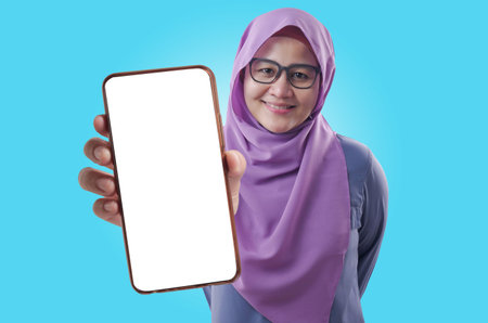 Young Asian muslim woman wearing hijab looking to camera, smiling and showing empty blank white copy space phone mock up templateの写真素材