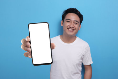 Young Asian man looking to camera, smiling and showing empty blank white copy space phone mock up templateの写真素材