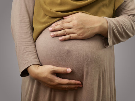 Muslim pregnant mother wearing hijab, anonymous mom holding her big belly, expecting newbornの写真素材