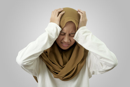 Portrait of sad young Asian muslim girl wearing hijab crying against red background, despression conceptの写真素材
