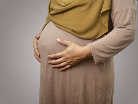 Muslim pregnant mother wearing hijab, anonymous mom holding her big belly, expecting newbornの写真素材