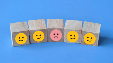 Sad face among happy faces, icon on wooden block cube, against blue backgroundの写真素材