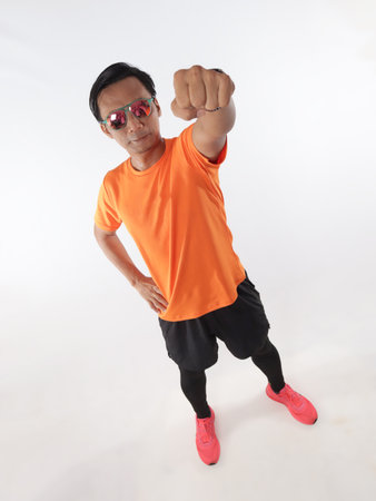 Strong confidence athletic young Asian male wearing running jersey looking at camera and showing power fist, top down full length studio shot portrait against white backgroundの写真素材
