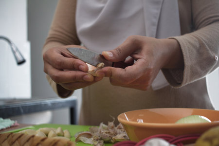 Cooking in kitchen. Asian muslim woman peeling, cutting and slicing onion and garlic. Preparing...