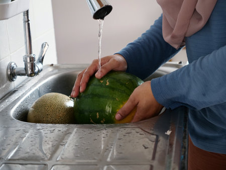 Asian muslim woman washing cleaning melon and watermelon fruits in kitchen sink, food preparationの写真素材