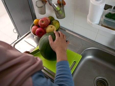 Asian muslim woman cutting slicing watermelon fruits in kitchen, food preparationの写真素材