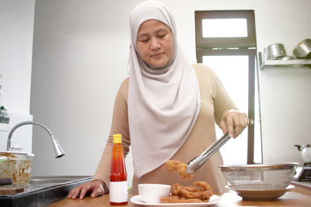 Asian muslim woman serving crispy fried chicken on white plate with ketchup or chili sauceの写真素材