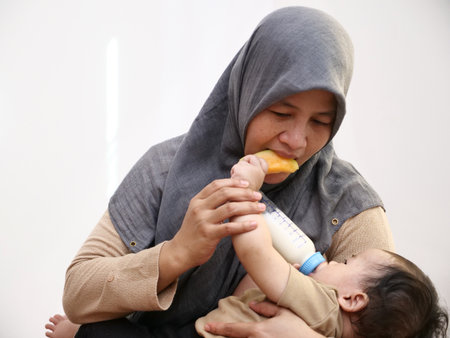 Asian muslim mother feed her baby with infant formula milk in bottle, happy joy love expressionの写真素材