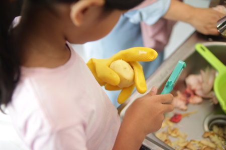 Mother and little girl daughter cooking in kitchen, making meal food preparation, cutting slicing chicken meat and potatoesの写真素材