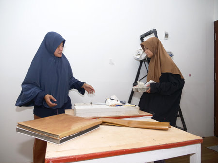 Two Asian muslim women, mother and daughter doing crafts work, covering table with wooden textured vinylの写真素材
