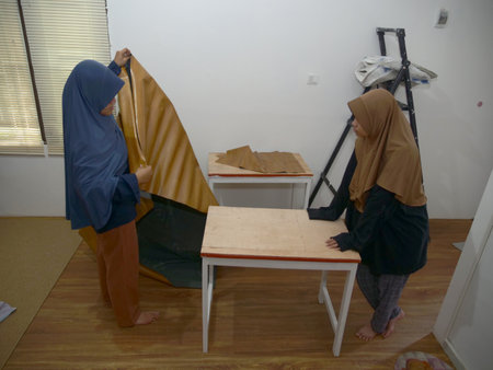 Two Asian muslim women, mother and daughter doing crafts work, covering table with wooden textured vinylの写真素材