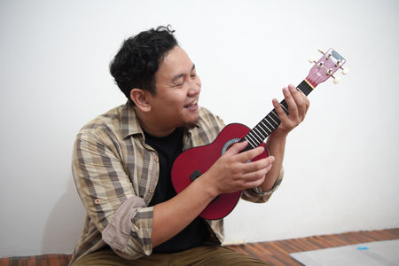 Asian man singing while playing ukulele at home