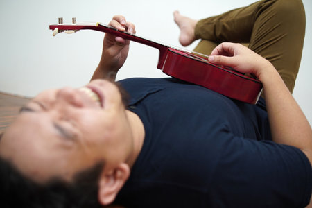 Asian man singing and playing ukulele at homeの写真素材