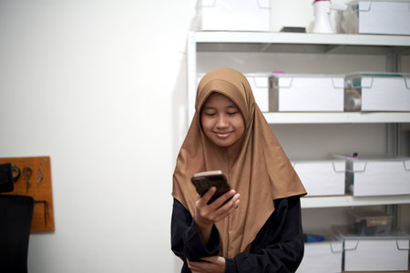 Young Asian muslim woman smiling when looking at her phone, happy expression, person receiving good newsの写真素材