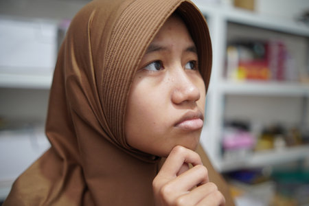 Young Asian muslim woman looking up with hand on chin, thinking or serious contemplation expressionの写真素材