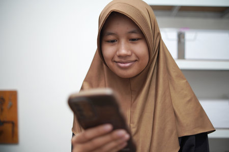 Young Asian muslim woman smiling when looking at her phone, happy expression, person receiving good newsの写真素材