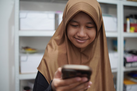 Young Asian muslim woman smiling when looking at her phone, happy expression, person receiving good newsの写真素材