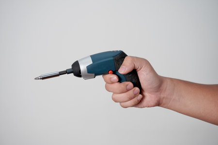 Male person hand holding electric power screwdriver, over grey backgroundの写真素材