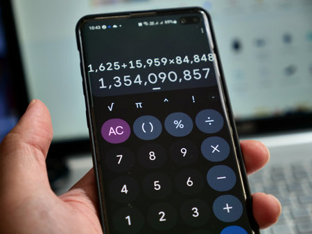 Hand holding smart phone with digital calculator app shown on its screen, accounting conceptの写真素材