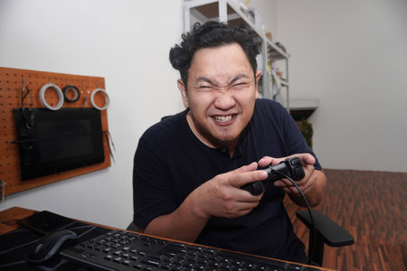 Adult Asian man playing video games on computer, happy smiling expression while holding game consoleの写真素材