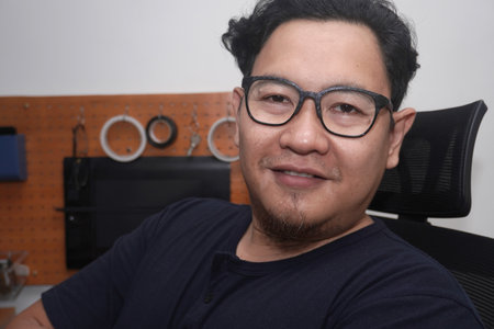 Adult Asian man wearing eyeglasses looking at camera and smiling. Successful entrepreneur working at...