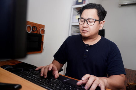 Adult Asian man typing on pc computer at home, freelancer working remotely, online job concept,...