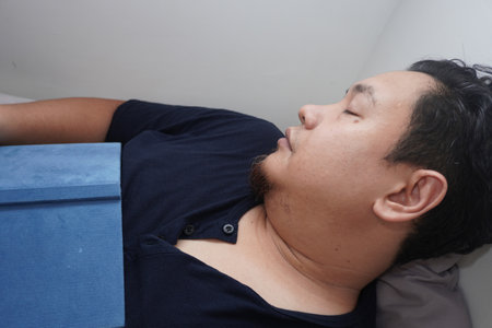 Adult Asian man sleep on bed mattress while holding book, tired relax person reading book