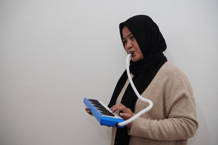 Asian muslim woman wearing hijab playing pianica, melodica blow organ musical intrumentの写真素材
