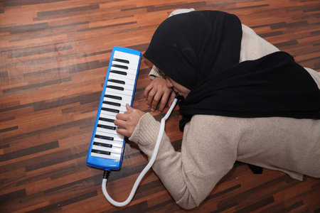 Asian muslim woman wearing hijab playing pianica while lying on floor, musical instrumentの写真素材