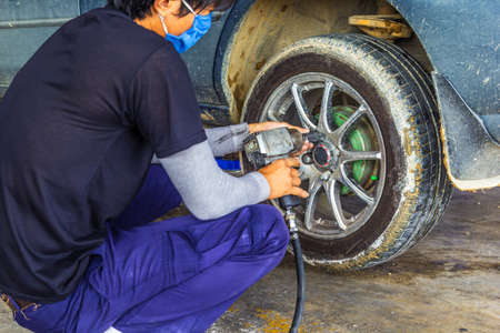 Car mechanic screwing or unscrewing car wheel of lifted の写真素材