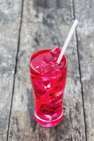 Red juice in a glass with ice on wooden tableの写真素材