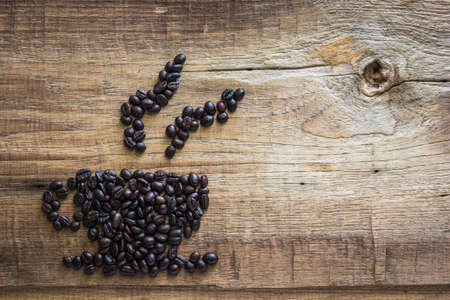 Roasted coffee beans placed in the shape of a cup on wooden tableの写真素材