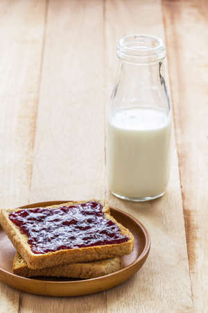 Toast with jam in wooden plate and milk bottle on wood tableの写真素材