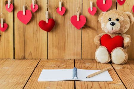 A photo of notepad on wood board with teddy bear holding heart sharp pillow background, Selective focusの写真素材