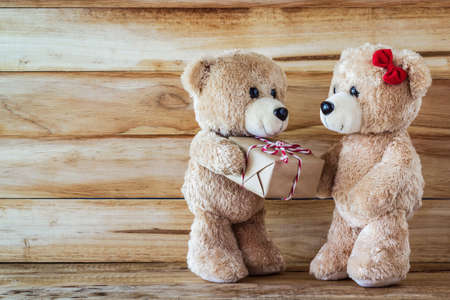 A photo of Teddy bear have a gift to girl friend with plank woodboard backgroundの写真素材