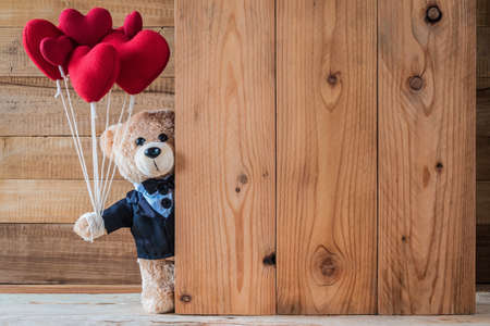 A photo of teddy bear holding heart-shaped balloon with wood board textureの写真素材