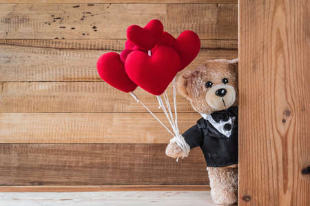 A photo of cute teddy bear holding heart-shaped balloon with wood board textureの写真素材