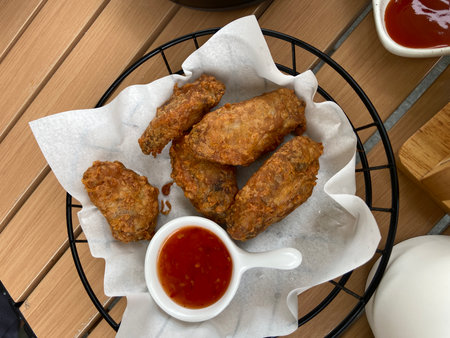 Fried chicken wings in a basket with sauce on a wooden tableの写真素材