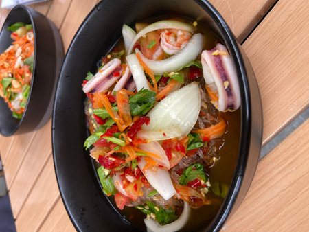 Thai spicy salad in black bowl on wooden table, Thai foodの写真素材