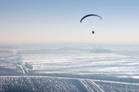 Aerial view of paramotor flying over the vastness of winter snowy French fields with horizon and blue skyの写真素材