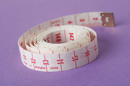 Measuring tape isolated on purple background and rolled up on itself