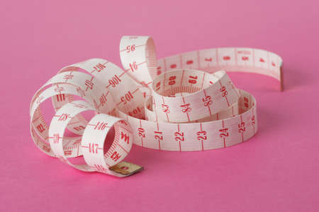 white and red dressmaker's ribbon wrapped around itself and isolated on pink backgroundの写真素材