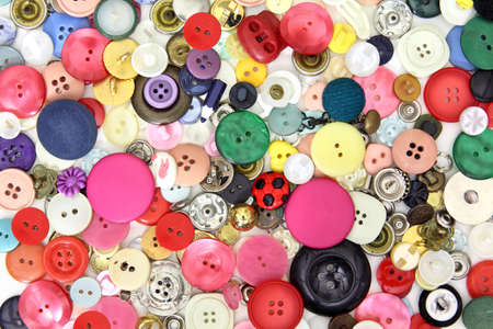 Set of buttons and sewing accessories in very different colors, sizes and shapes. Predominantly pink and red and some yellow, blue and green buttonsの写真素材