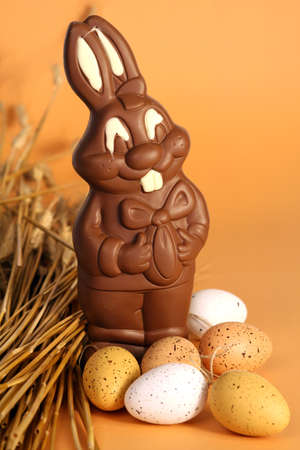 Big chocolate Easter bunny with eggs and ears of wheat on orange backgroundの写真素材